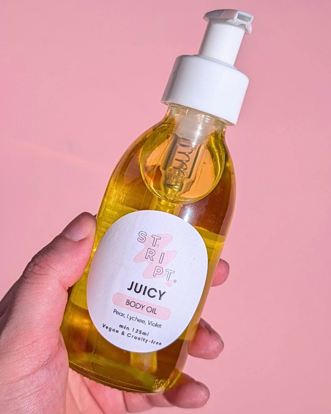 Juicy Body Oil by Stript Cosmetics | Handmade, Vegan Body Care | Hand holding a glass bottle with white label and white pump